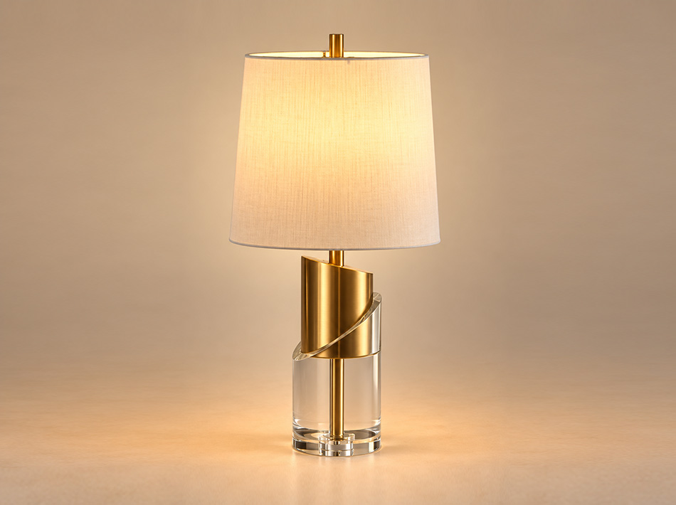Embrace brushed gold table lamp with clear cylindrical man-made crystal base, curved gold metal detailing and white linen shade.
