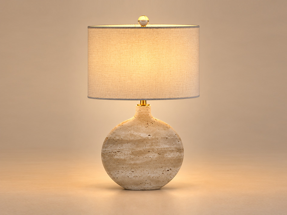 Tavi brushed gold table lamp with a rounded beige Classico travertine base, oval beige fabric shade and clear decorative crystal-style finial.